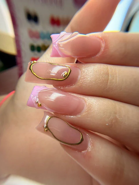 Primer plano de uñas rosas con pétalos en relieve y líneas doradas